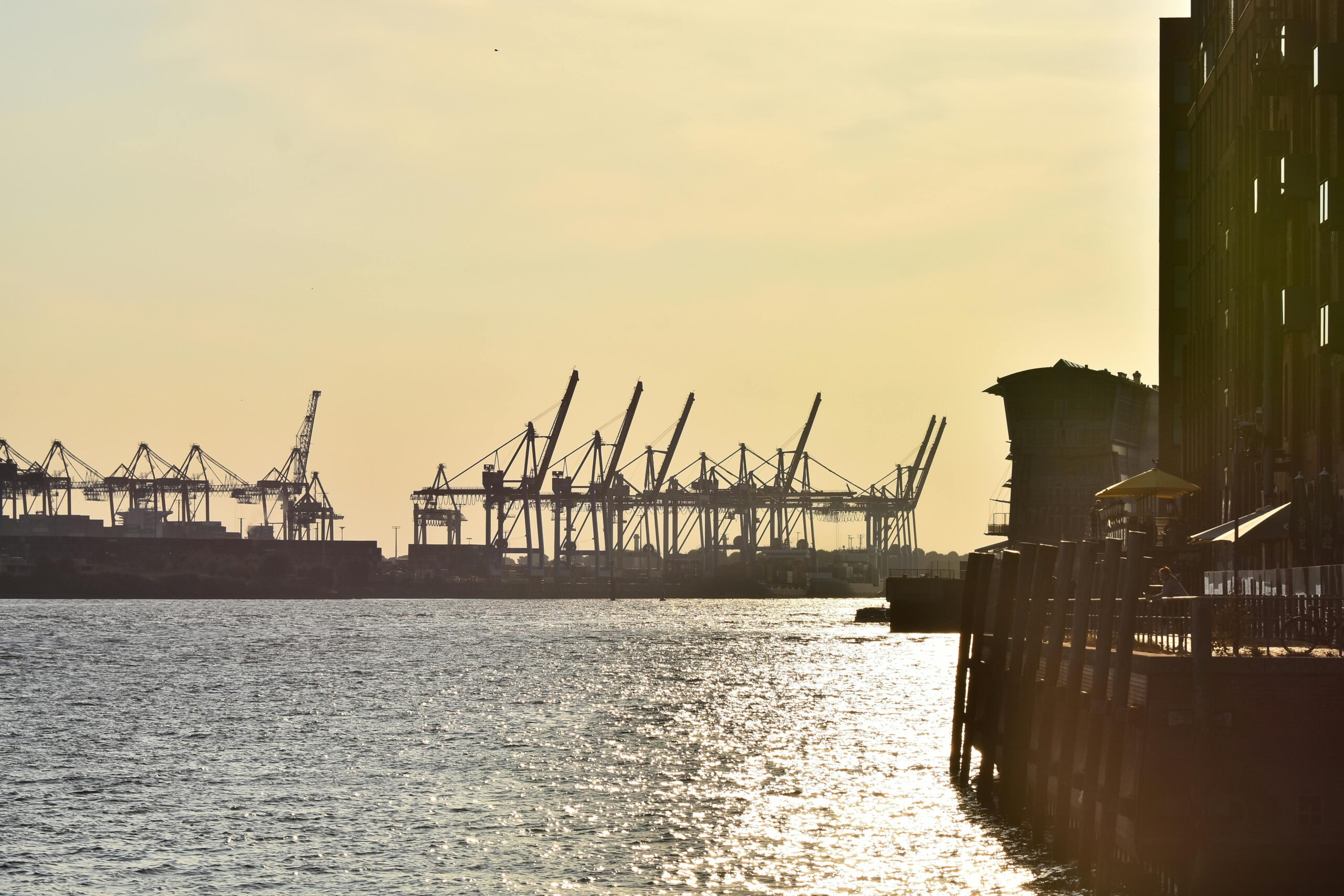 A serene view of a commercial harbor during dusk with cranes silhouetted against the sky.